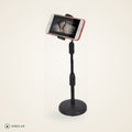 Suporte de mesa para celular preto com base redonda, segurando o celular na horizontal